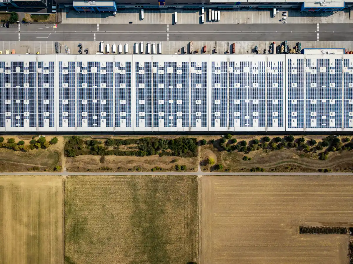 Copertura di un capannone interamente rivestita di moduli, accanto a campi coltivati